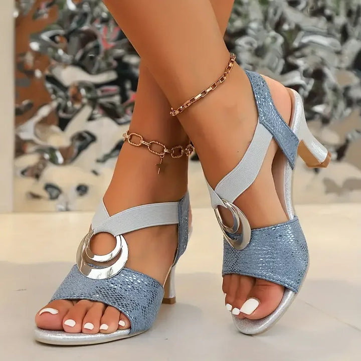 Blue high-heel sandals with open toe, ankle strap, and large silver ring hardware.